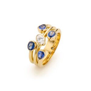 Auxane ring in 18K yellow gold featuring an oval diamond surrounded by pear- and oval-shaped blue sapphires in a bold multi-band design.